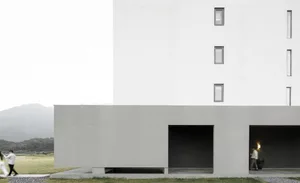Modern minimalist building with a white facade and concrete structure, featuring a geometric design and small windows.