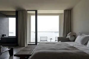 A minimalist bedroom with a large bed, stone walls, and fabric textiles.