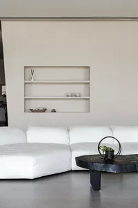 A minimalist living room with a large white sofa and a black coffee table on a concrete floor.