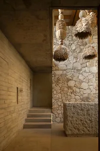 Concrete corridor with stone wall and ceiling, featuring thatched lighting fixtures and wooden steps.