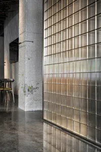 Industrial-themed restaurant interior with concrete flooring and large glass paneling walls.
