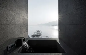 A modern stone relaxation bath overlooking a serene lake and mountains.