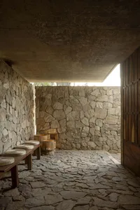 A stone-walled interior with wooden furniture and baskets on a stone-paved floor.