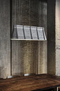 A metal cylindrical pendant light fixture hanging from a concrete wall.