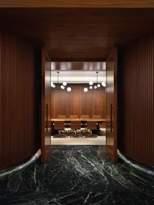 A modern conference room with wooden paneling and marble furniture, featuring a long table surrounded by chairs and illuminat