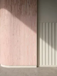 A modern interior design featuring a textured marble wall with vertical lines and shadows created by sunlight.