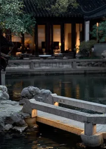 A serene garden scene featuring a stone bridge over water, with a traditional Chinese building in the background.