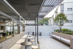 A minimalist cafeteria with concrete walls, tables, and chairs, featuring industrial-style furniture and a large window for n