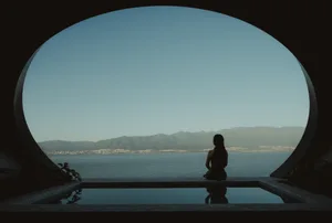 A minimalist setting featuring a stone structure looking out to a scenic view of the sea and mountains.