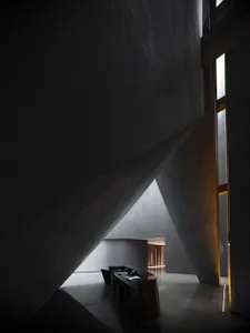 A minimalist hotel reception area with concrete walls and a sleek, black reception desk.