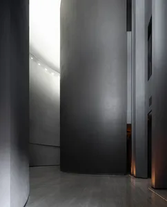A modern, minimalist interior space with a textured concrete wall and floor, illuminated by recessed lighting.