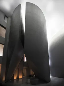 A modern monolithic concrete interior with large, curved, dark-gray walls and a geometric staircase.