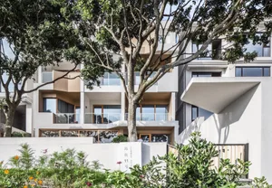 A modern residential building with a sandstone exterior and large trees in the foreground.