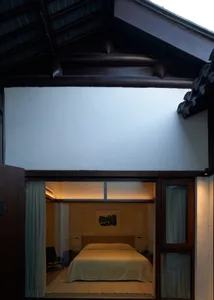 Minimalist bedroom with a double bed, white bedding, a wooden headboard, and white walls.