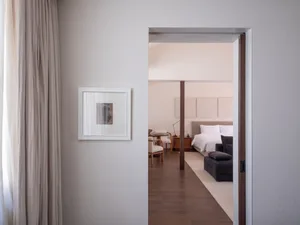 A minimalist bedroom with a white bed, beige curtains, and wooden flooring.