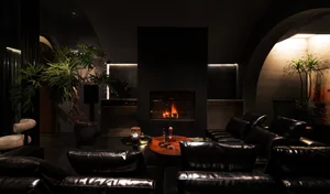 A modern living room with black leather furniture and a warm fireplace.