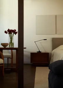 Modern, minimalist bedroom with wooden furniture and a vase of red flowers on a table.