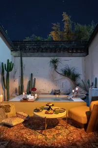 An indoor spa area with a concrete bathtub, candles, and cactus plants under a starry sky.