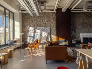 An industrial-style living room with concrete, stone, and metal surfaces, featuring modern furniture and exposed ductwork.