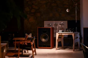 A wooden studio speaker and recording equipment in a dimly lit room with stone walls.