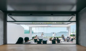 People sitting near a large glass window overlooking the ocean and mountains.