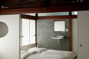 A small, minimalist bedroom with a concrete wall and white bedding.