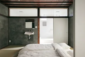 A minimalist bedroom with a concrete wall and floor, featuring a white bed and sink.