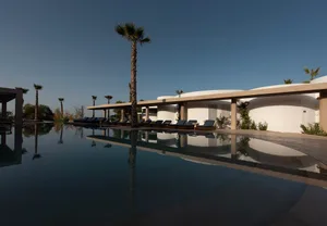 A minimalistic resort with glass walls, surrounded by greenery and palm trees.