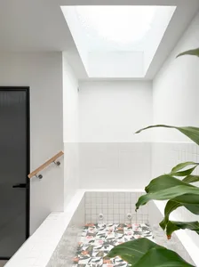 A modern bathroom featuring white tiled walls, a patterned floral tile floor, and a skylight with glass blocks