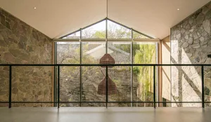 A modern interior design featuring a glass window with a view of trees and a stone wall.