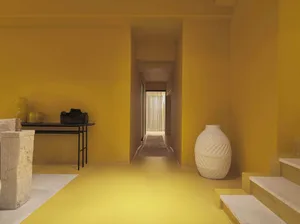 A minimalist interior space featuring a concrete floor and walls, with a white vase and a black table with decorative items.