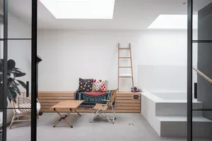 A modern, open-plan living space featuring a wooden bench, fabric-covered seating, and white tiled flooring.