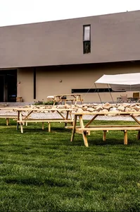 An outdoor event space featuring wooden tables and picnic benches on a grassy area.