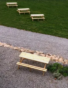 Four wooden picnic benches placed outdoors on a gravel surface surrounded by rocks and grass.