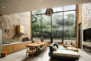 A modern industrial living room with a wooden table and green sofa overlooking a forest.