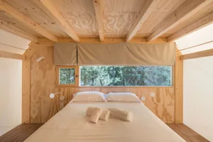 A modern, minimalist bedroom with wooden elements and a large window overlooking a forested area.