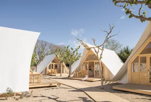 Modern campsite architecture featuring white canvas tents with wooden structures and minimalistic design.
