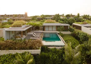 Modern outdoor living space with natural earth tones, featuring a pool, lounge chairs, and greenery.