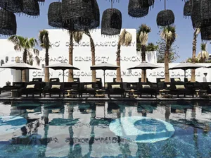 A modern poolside lounge area with black lounge chairs, umbrellas, and palm trees.
