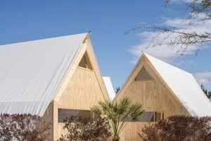 A modern residential tent with a triangular roof made of light-colored wood and covered with a white fabric roof.