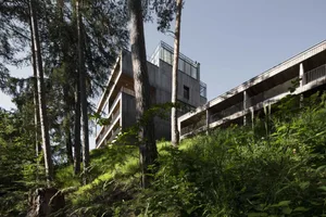 Modern residential building with wooden exterior and glass windows surrounded by trees and greenery.
