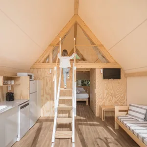 A small cabin interior with wooden paneling and a loft space accessed via a ladder. Features a kitchenette, seating area, and