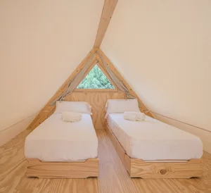 A minimalist bedroom with triangle-shaped windows, featuring twin beds with white bedding and natural wooden elements.
