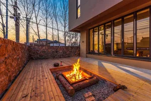 A fire pit surrounded by a wooden deck and stone wall, with a building in the background.