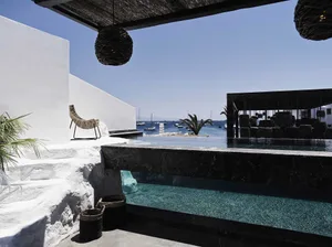 Concrete and marble vacation poolside area with lounge chairs and boats in the background.