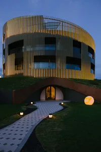 A modern, curved metal-clad commercial building with illuminated pathways at dusk.