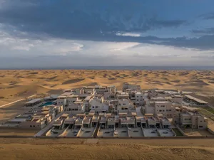 Aerial view of a resort complex in the desert, featuring numerous buildings and structures made of sand.