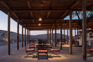 Wooden pergola with tables and chairs under a shaded area in a desert setting