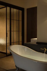 A minimalist bathroom with a white freestanding bathtub and a textured frosted glass sliding door.