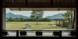 A minimalist restaurant interior with wooden elements and a view of a paddy field and mountains.